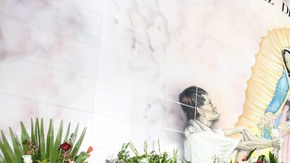 Docenas de arreglos florales dejados como ofrenda ante una imagen de la virgen en una pared de la Iglesia de La Placita.