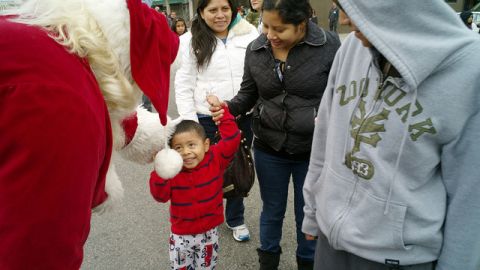 Un Santa Claus en Skid Row saluda a un menor y a su familia, que se forman en la fila para recibir regalos de la Misión Jordan.