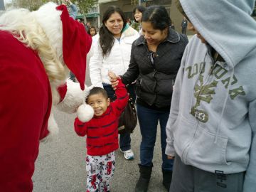 Un Santa Claus en Skid Row saluda a un menor y a su familia, que se forman en la fila para recibir regalos de la Misión Jordan.