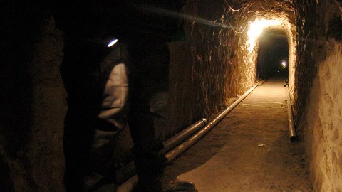 Un policía mexicano enciende  su linterna para mostrar el interior de este  túnel que tiene  3798 pies de largo,   que pasa de México a EE.UU. por el sur de California.