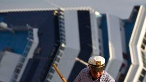 Un hombre barre la acera con el crucero Costa Concordia al fondo, todavía escorado cerca de la costa de la isla de Giglio.