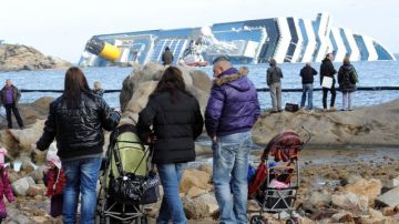 Varias personas observan el crucero Costa Concordia, de donde hoy fue sacado el cuerpo de una mujer.