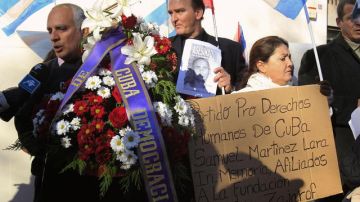 El portavoz de la Plataforma Cuba Democracia Ya, Rigoberto Carceller (i), sujeta una corona de flores durante la concentración ante la embajada de Cuba en Madrid por la muerte del disidente cubano Wilman Villar.