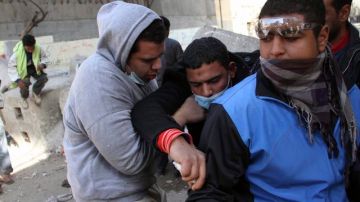 Varios manifestantes egipcios ayudan a un compañero afectado por gas lacrimógeno en enfrentamientos con fuerzas de seguridad.