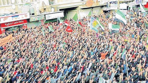 Sirios con sus armas en alto y banderas revolucionarias ondeando durante una protesta convocada en la Plaza del Reloj de Idlib (Siria).