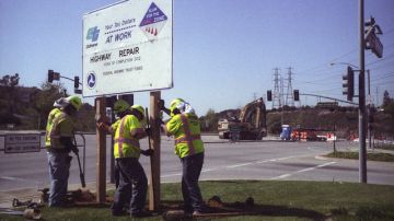 Trabajadores instalan el letrero  anunciando el inicio de la reparación del puente dañado por incendio en la carretera 60 en Montebello.