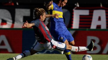 Jonathan Botinelli (izq.),  de San Lorenzo, se barre para desarmar la jugada de Pablo Mouche, del Boca Juniors, que sigue invicto y líder.