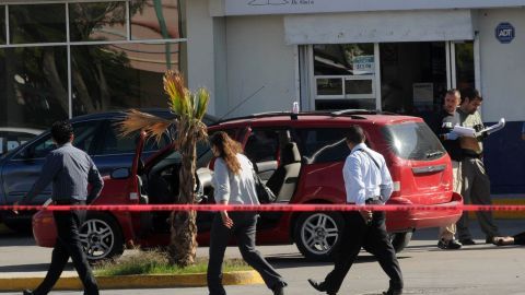 Un grupo de forenses (d)  inspeccionan el cuerpo de una mujer que fue asesinada por un grupo de desconocidos cuando circulaba en su vehículo en Ciudad Juárez.
