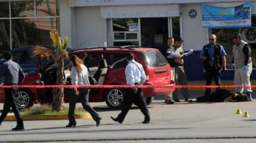 Un grupo de forenses (d)  inspeccionan el cuerpo de una mujer que fue asesinada por un grupo de desconocidos cuando circulaba en su vehículo en Ciudad Juárez.