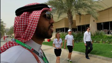El piloto alemán Nico Rosberg (der.) camina con amigos por el jardín cerca de un reportero vestido a la usanza arábe ayer en Bahrein.