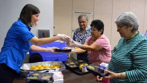 Wilda Belisle, directora de los Clubes de Comidas de Adultos y Comidas sobre Ruedas reparte alimentos a Alicia Cely (der.), Ruth Illescas y Herminia García.