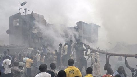 Nigerianos ayudan a sostener una manguera para apagar las llamas en el lugar donde quedaron los escombros de un avión comercial que se estrelló con 159 personas a bordo en Lagos, Nigeria.