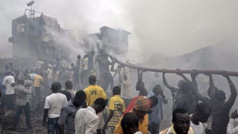 Nigerianos ayudan a sostener una manguera para apagar las llamas en el lugar donde quedaron los escombros de un avión comercial que se estrelló con 159 personas a bordo en Lagos, Nigeria.