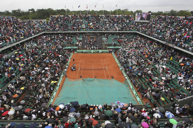 Empleados del Roland Garros cubren la cancha con la lona impermeable mientras el público busca la salida.
