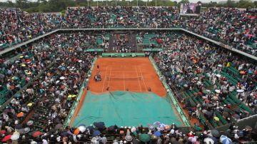 Empleados del Roland Garros cubren la cancha con la lona impermeable mientras el público busca la salida.