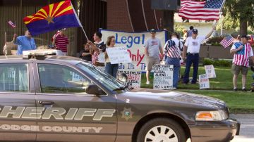 En esta foto de archivo, un vehículo del alguacil pasa frente a un grupo de personas que se manifestaban contra los inmigrantes ilegales, afuera del ayuntamiento de Fremont, Nebraska.