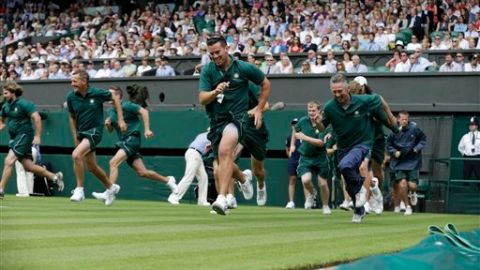 Personal de Wimbledon corre para colocar la lona de plástico sobre el césped de las canchas.