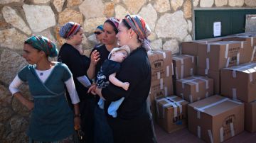 Mujeres judías observan a los  empleados  que fueron contratados por el Gobierno para remover  pertenencias del que había sido el hogar de estas en Israel.