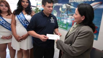 Salvador Segura,  del comité de Sunzeños  da  un cheque  a Juanita Vigil  para pagar parte de los  boletos de avión.