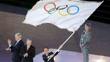El alcalde de Río de Janeiro, Eduardo Paes, ondea la bandera olímpica tras recibirla de manos del alcalde de Londres, Boris Johnson.