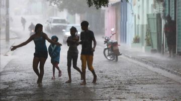 Niños caminan bajo la intensa lluvia, durante el paso de la tormenta tropical "Isaac" en Enriquillo, República Dominicana.