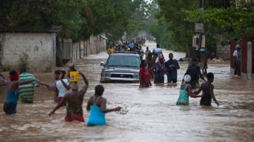 Residentes de Puerto Príncipe, capital de Haití, tratan de cruzar por una de las muchas calles anegadas que dejó la tormenta.