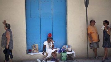 Una mujer vestida con un traje típico habla con turistas en una calle de La Habana.