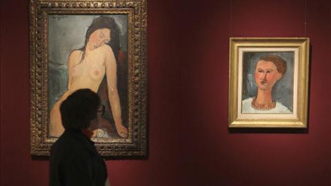 Una mujer contempla dos cuadros del pintor francés Amadeo Modigliani " Mujer sentada" (i) y "Retrato de un joven".