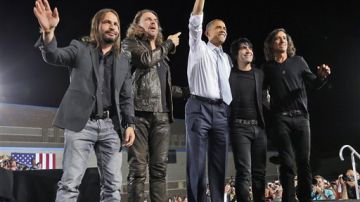 El presidente Barack Obama saluda a la gente acompañado en el estrado de los miembros de la banda mexicana de rock Maná, durante un acto de campaña en la secundaria Desert Pines, el domingo 30 de septiembre de 2012 en Las Vegas.