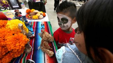 Dos  menores con las caras pintadas miran entretenidos las mesas con los altares levantados por el Día de los Muertos en el Centro del Pueblo, mientras los adultos  aprovechan para inscribirse  para votar.
