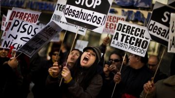 Un manifestante sostiene una pancarta que dice "Stop desahucios" en una protesta hoy en frente de la sede del Partido Popular en Madrid.