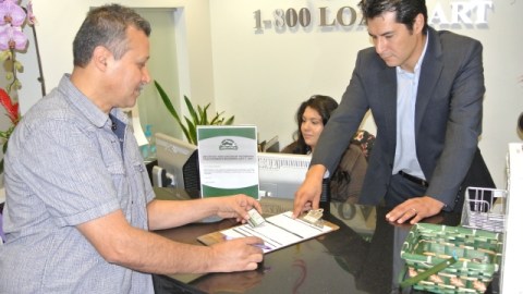 Oscar Rodríguez, de LoanMart, explica a Rodolfo Santana los términos de un préstamo sobre el título de su auto.