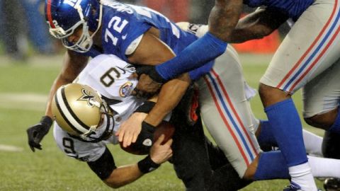Drew Brees de Nueva Orleans es derribado por Osi Umenyiora de Nueva York.