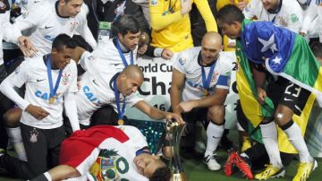 El peruano Paolo Guerrero posa envuelto en una bandera de su país, mientras sus compañeros del Corinthians admiran el trofeo de campeones mundiales.