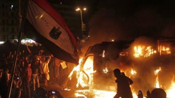 Manifestantes egipcios  frente a vehículo de las fuerzas de seguridad en llamas, mientras  disturbios siguen en el  El Cairo, a pesar de las medidas de emergencias y toque de queda que ordenó el Presidente.