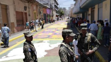 Militares vigilan mientras centenares de jóvenes y adultos trabajan en diseños de alfombras de serrín, en Tegucigalpa, Honduras, como parte de las actividades de Semana Santa.