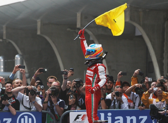 Fernando Alonso alza el banderín de su escudería desde el podio.