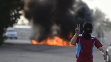 Un ciudadano bareiní hace la señal de la victoria frente a varios neumáticos en llamas durante una protesta contra la F1.