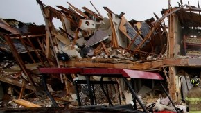 Un coche severamente dañado se observa enfrente de un edifico de departamentos totalmente destruído como resultado de la explosión mientras  rescatistas inspeccionan el lugar en West, Texas.
