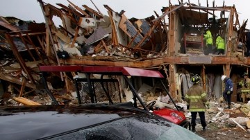 Un coche severamente dañado se observa enfrente de un edifico de departamentos totalmente destruído como resultado de la explosión mientras  rescatistas inspeccionan el lugar en West, Texas.
