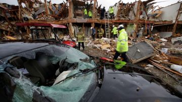 Un coche severamente dañado se observa enfrente de un edifico de departamentos totalmente destruído como resultado de la explosión mientras  rescatistas inspeccionan el lugar en West, Texas.