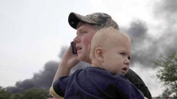 Mark Paugh carga a su hijo de 15 meses mientras observa el humo producto de la explosión del tranvía.