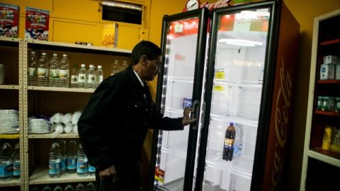 Un hombre abre una nevera casi vacía, mientras realiza compras en un abasto, en Caracas, Venezuela.