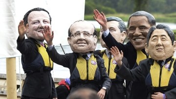 Manifestantes con máscaras de líderes del G8 saludan a la policía durante una manifestación.