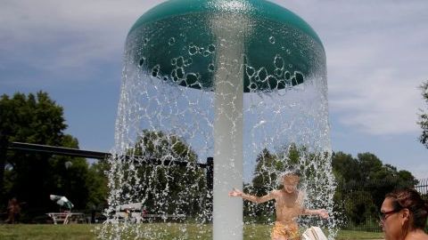 Pamela Liu se pone al día en su lectura mientras su hijo Jayden, juega en una fuente  en Southside Park en Sacramento, California.
