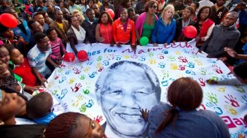 Personas cargan una enorme pancarta deseando recuperación a Nelson Mandela, fuera de la clínica donde está internado.