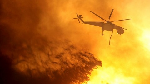 Un helicóptero echa agua sobre las llamas que parecen no dar tregua a los bomberos.  Más personas se han visto  obligadas a dejar sus hogares a concecuencia de la expansión del fuego.