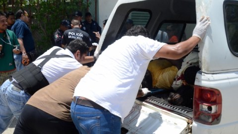 Empleados de la Oficina del Forense recogen los cuerpos de individuos acribillados.