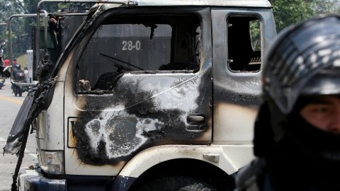 Un miembro del escuadrón antimotines permanece  cerca de un vehículo incinerado tras choques con campesinos.
