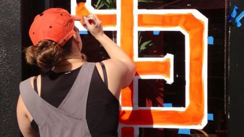 Una chica pinta las ventanas de un negocio con las iniciales de los Gigantes de San Francisco.